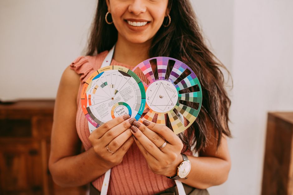 Smiling woman holding vibrant color wheel palettes indoors, showcasing creative design inspiration.